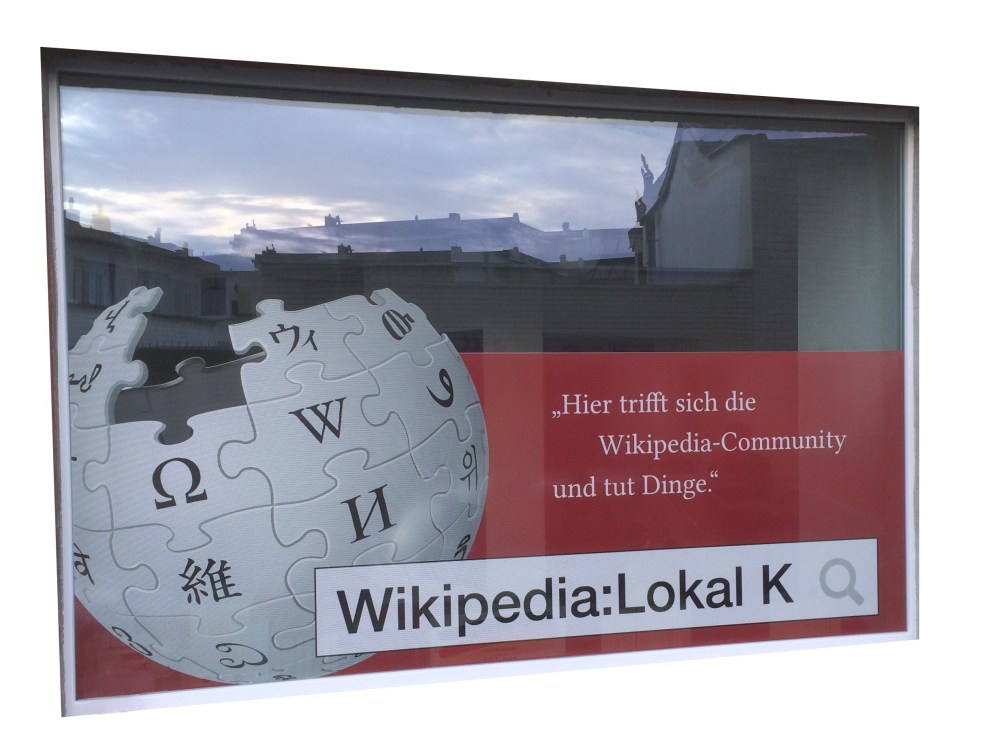 Das Schaufenster des Lokal K zeigt ein Puzzle in Form einer Weltkugel. Auf jedem Puzzle steht ein Buchstabe in unterschiedlichen Sprachen. Rechts daneben ist der Slogan des Lokals zu lesen.