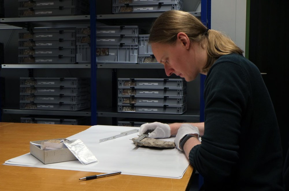 Seitliche Aufnahme eines Mitarbeiters, der einen Fund mit einem Messgerät untersucht.