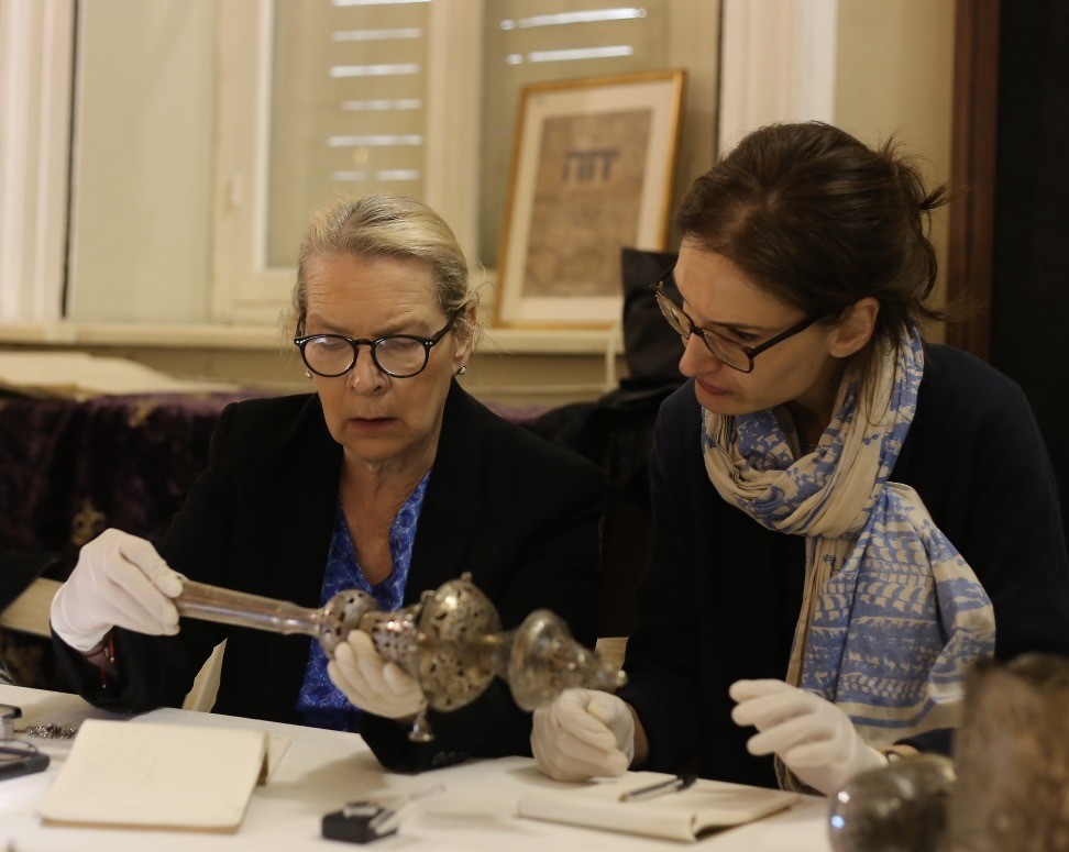 Zwei Frauen tragen weiße Handschuhe zum Schutz des Objektes. Frau Gogel hält das Objekt in beiden Händen.