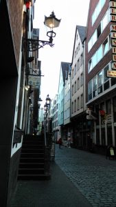 Eine enge Gasse, gesäumt von schmalen Häusern. In der Mitte Pflastersteine.