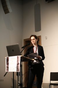 Vortragende am Stehpult vor einem Laptop.