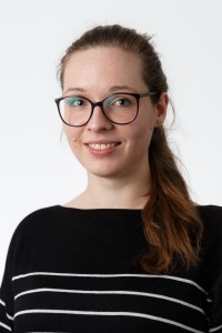 Portraitbild der lächelnden Carina Thomas. Sie trägt eine Brille mit einem schwarzen Gestell. Ihr langer Zopf liegt über ihrer linken Schulter.