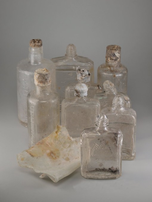 Fundobjekte aus der Grabung. Dabei handelt es sich um 9 Glasflaschen von Farina ohne Inhalt.
