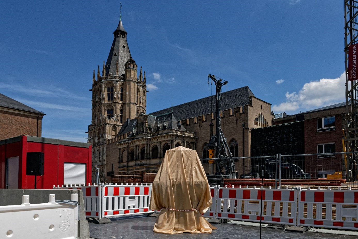 Im Hintergrund das Rathaus, davor die Baustelle mit dem verhüllten Grundstein.
