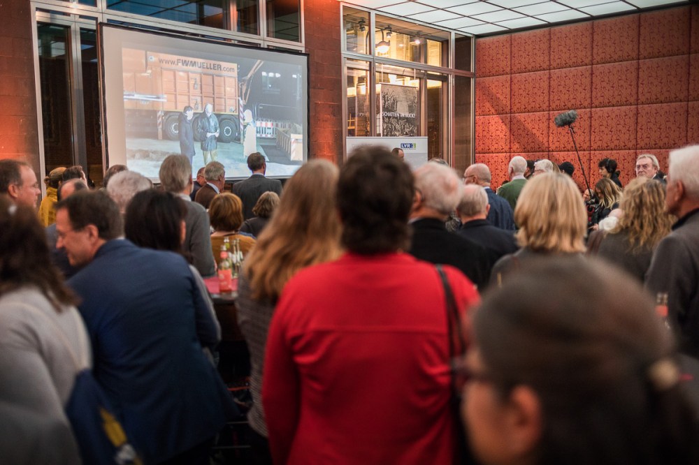 Die Gäste im Museum verfolgen das Geschehen auf der Baustelle auf einer Leinwand-Übertragung.