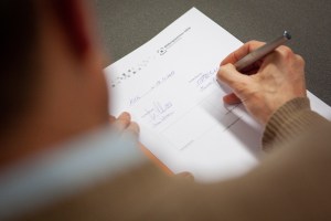 Im Vordergrund verschwommen die Schulter des MiQua-Direktors, im Bildzentrum die Kooperationsvereinbarung, die Thomas Otten gerade unterschreibt.