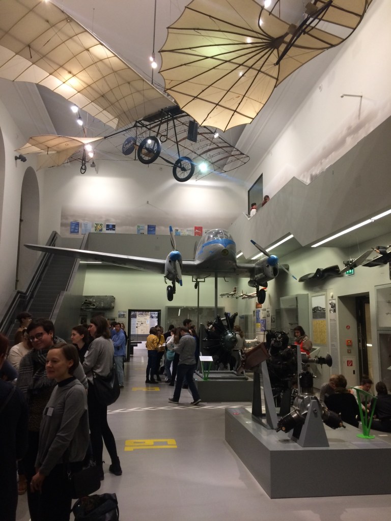 Der Ausstellungsraum im Verkehrsmuseum Dresden ist für das gettogether gut gefüllt mit Teilnehmer*innen der Tagung. Große Objekte wie beispielsweise Flugmaschinen hängen von der Decke und bestimmen so den Eindruck des Raumes.