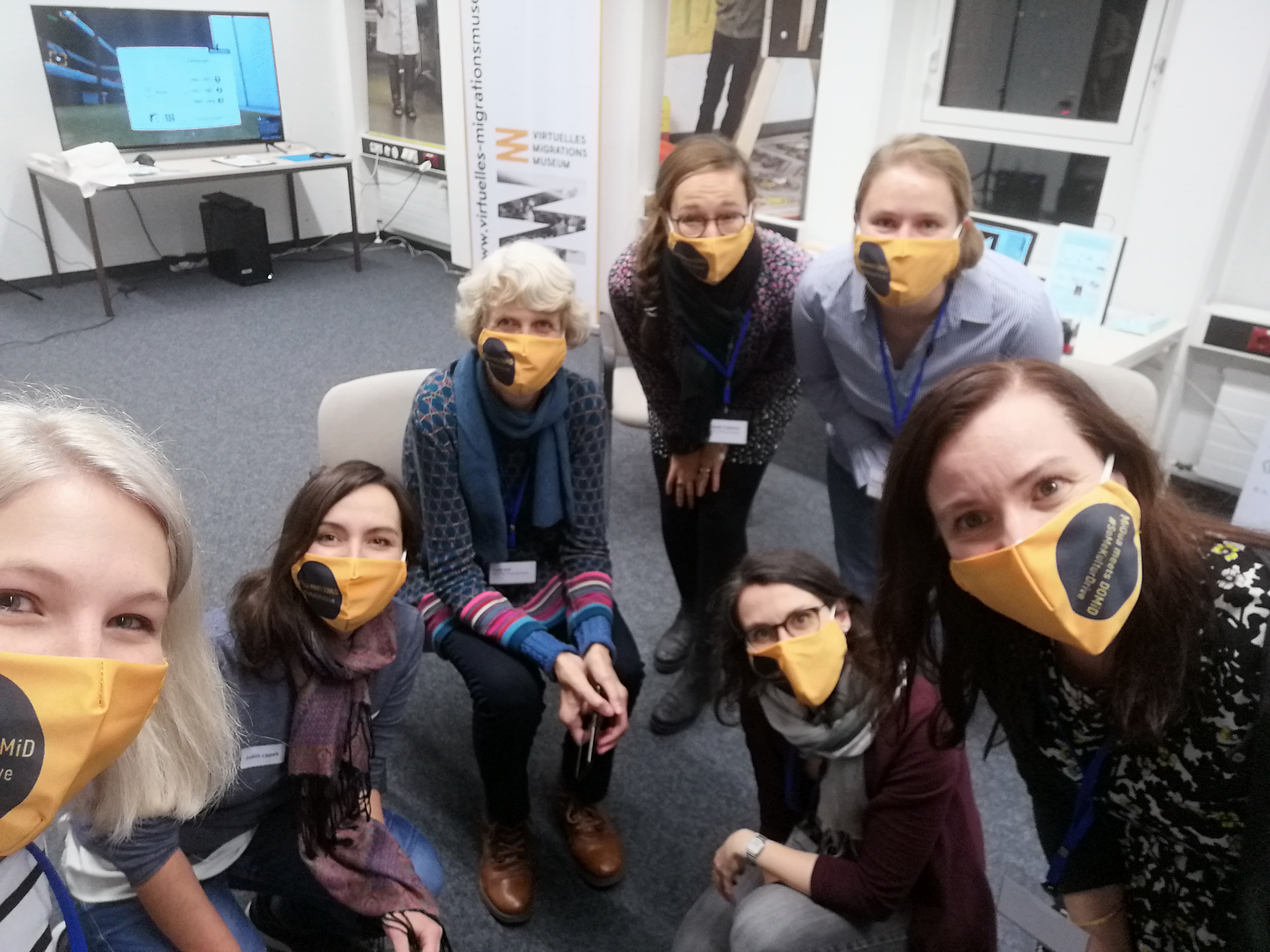 Ein Selfie vom Organisationsteam zum Abschluss der Veranstaltung. Die 7 Organisatorinnen lächeln mit unseren Masken im Veranstaltungsdesign in die Kamera.