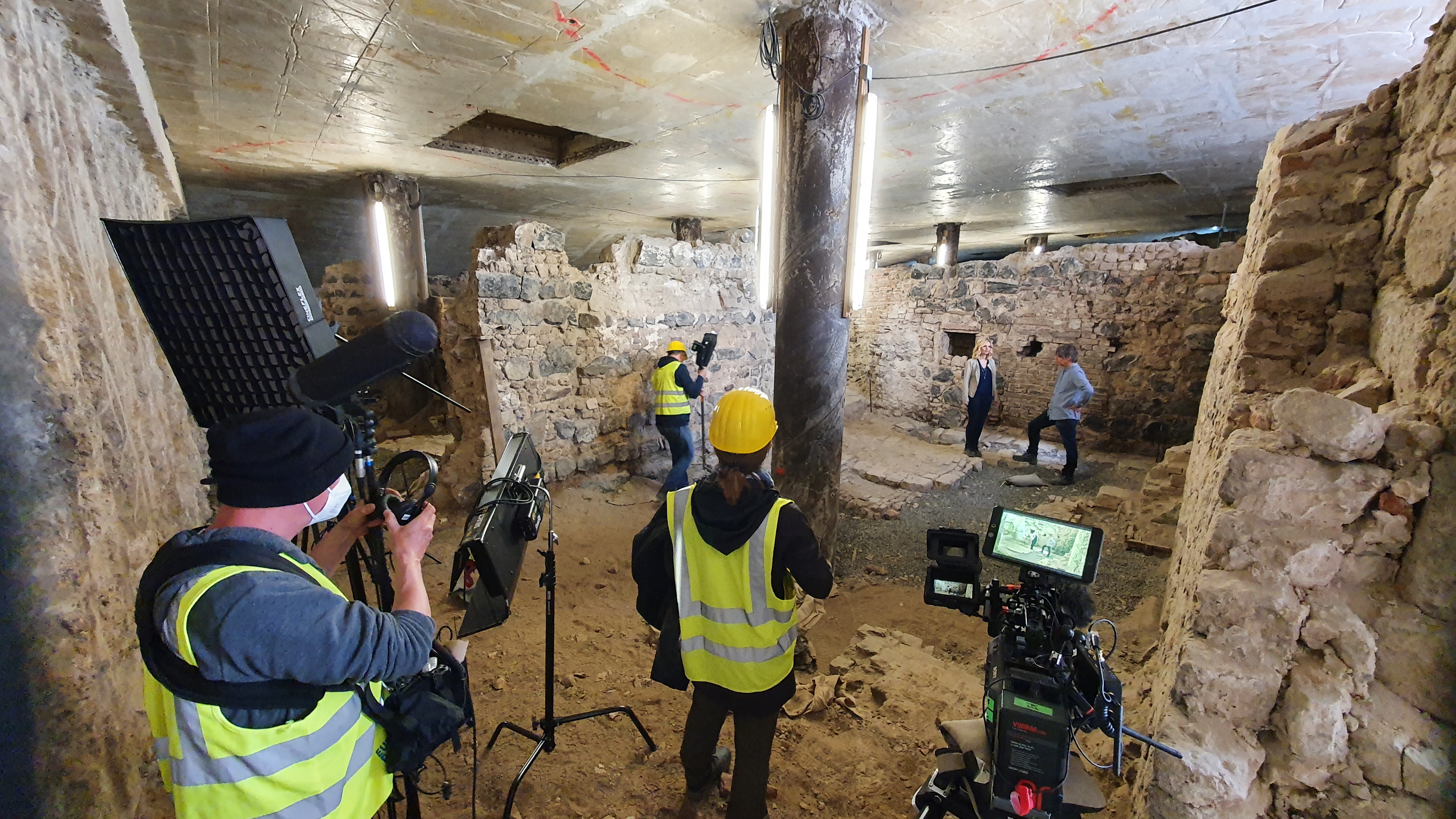 Das Bild zeigt die Situation der Filmaufnahme: Das Kamerateam mit Equipment nimmt das Interview mitten in archäologischen Befunden auf.