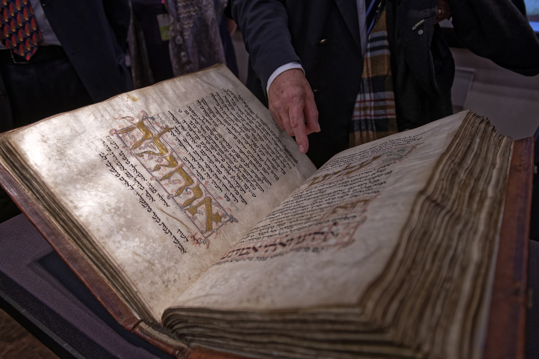 Die mittelalterliche Handschrift Amsterdam Machsor mit hebräischer Schrift und Illustrationen liegt aufgeklappt auf einem Tisch. Eine Hand zeigt auf ein Detail im Buch.