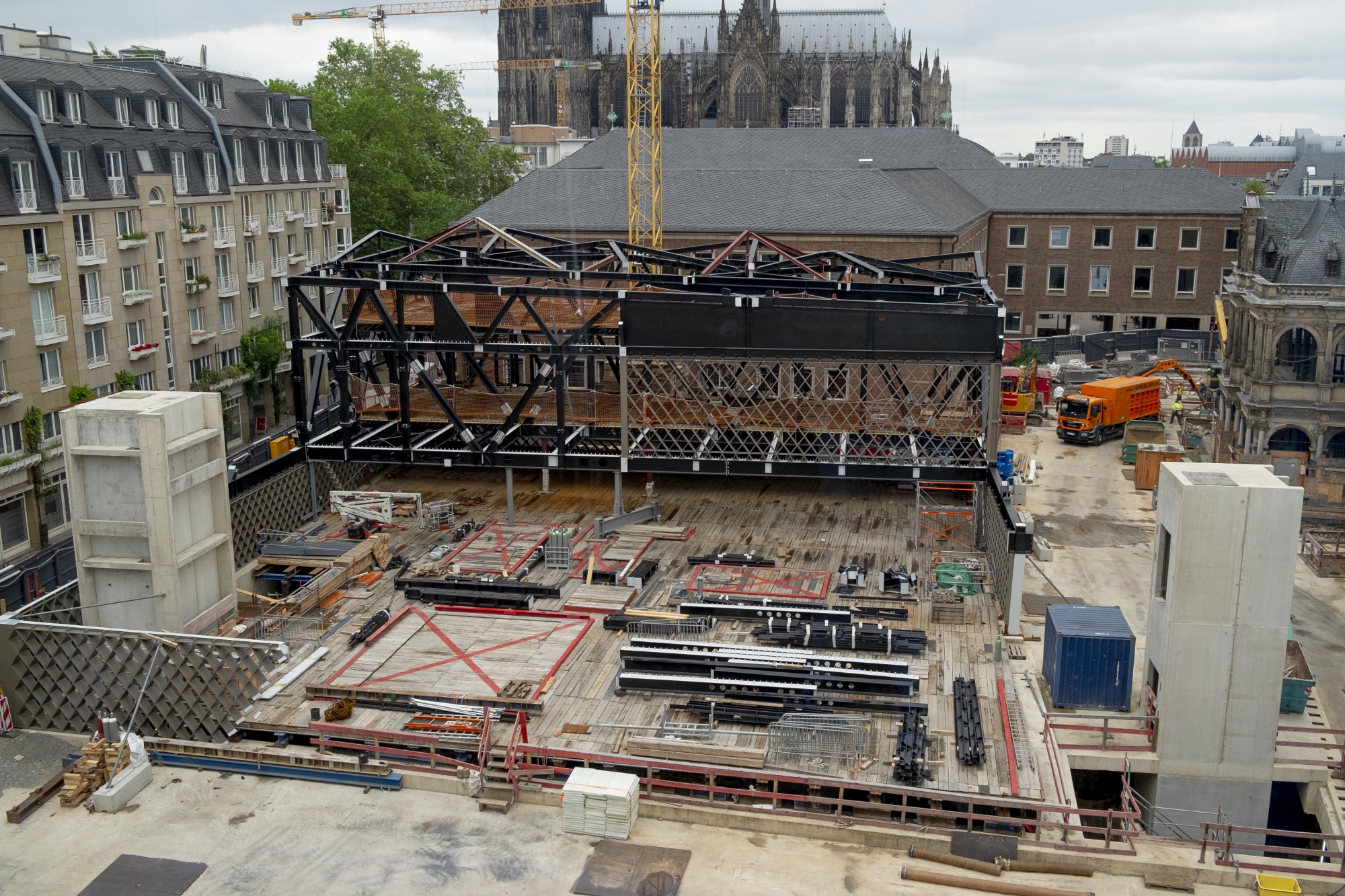 Die gesamte MiQua-Baustelle auf einem Bild: in der Mitte die Stahlkonstruktionen des späteren Museumsbaus, drum herum die Rautentragwerke aus Stahl durch die später auch von außen schon ins Museum hineingeschaut werden kann. Vorne im Bild links und rechts die späteren Aufzugschächte als helle Betonsäulen.