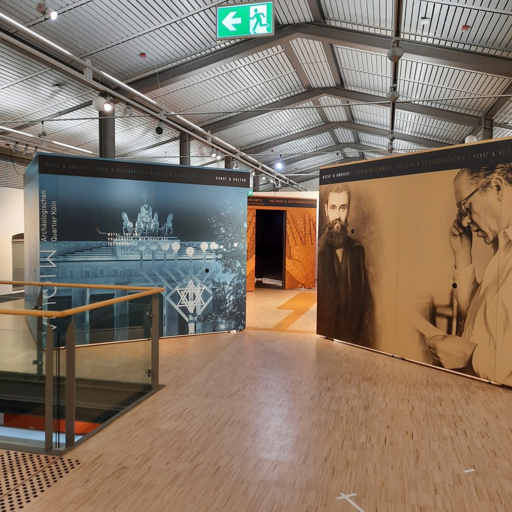 Blick in den Ausstellungsraum: Drei der vier Kuben sind auf diesem Bild unter grauem Dach zu sehen.