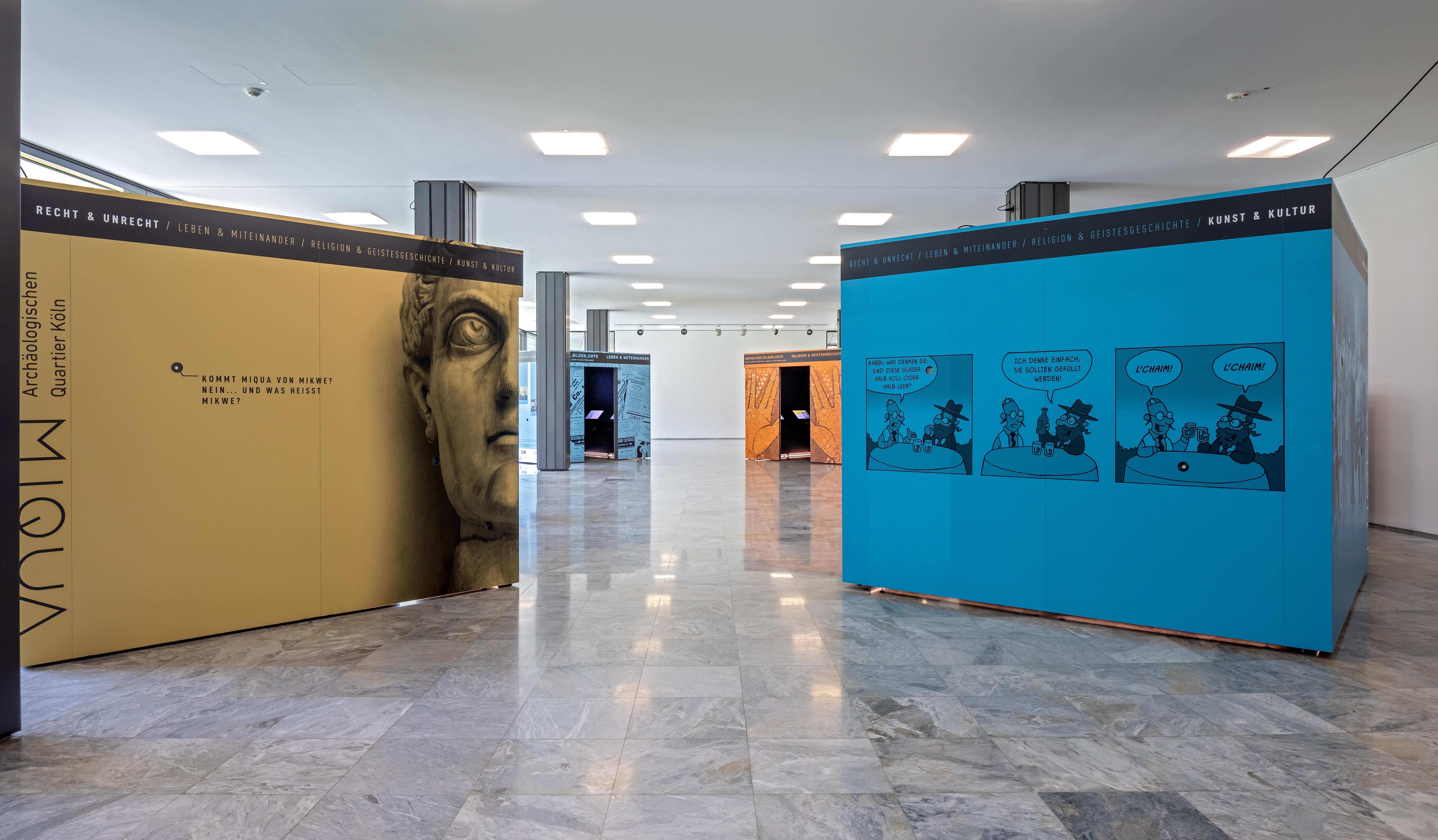 Im lichtdurchfluteten Foyer des Landeshauses stehen die vier Ausstellungskuben in den Farben gelb, blau, orange und dunkelblau.