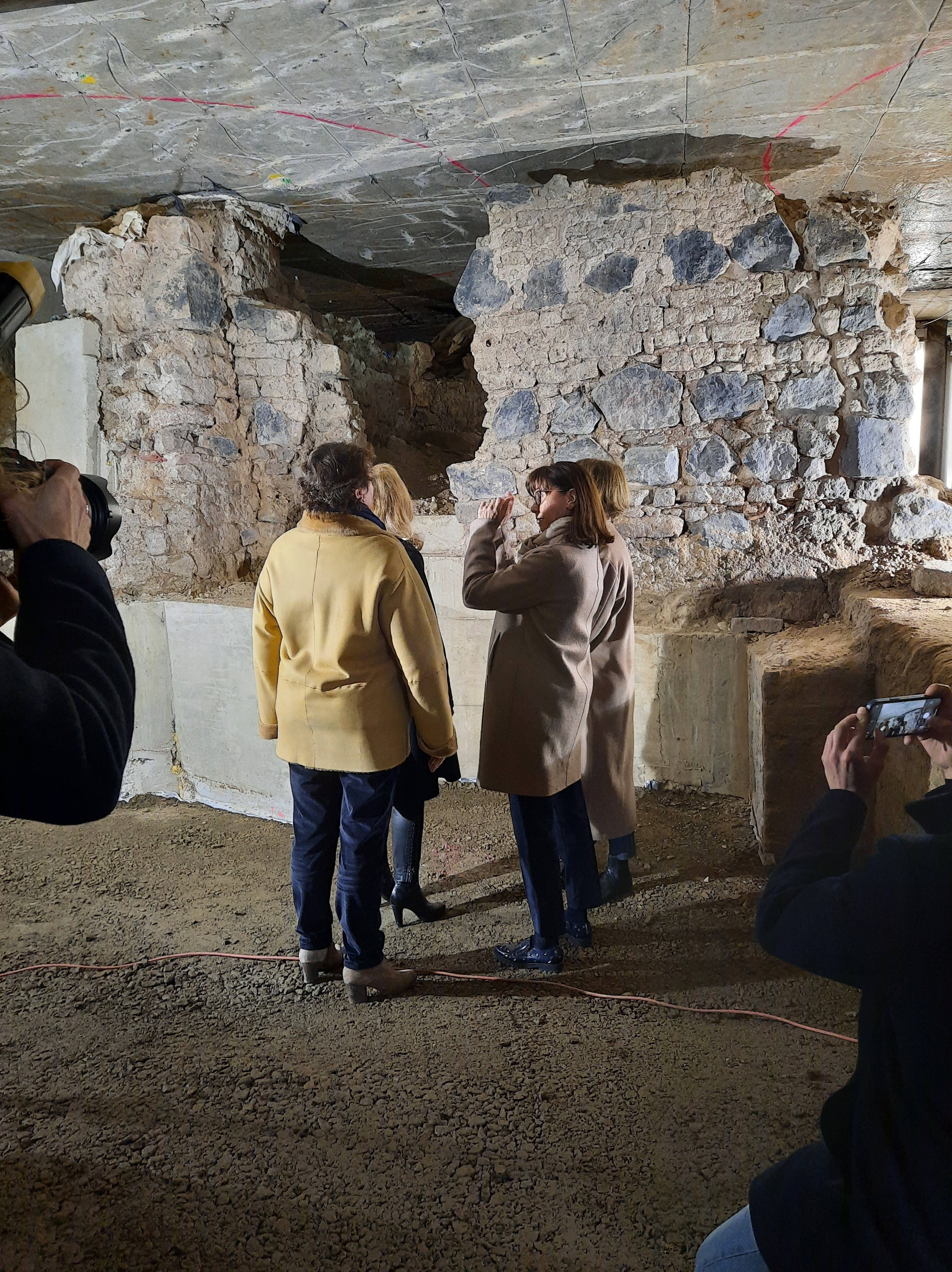 Im Bildzentrum: Vier Frauen, die sich die umgebenden archäologischen Befunde anschauen. Im Vordergrund zwei Fotografen.
