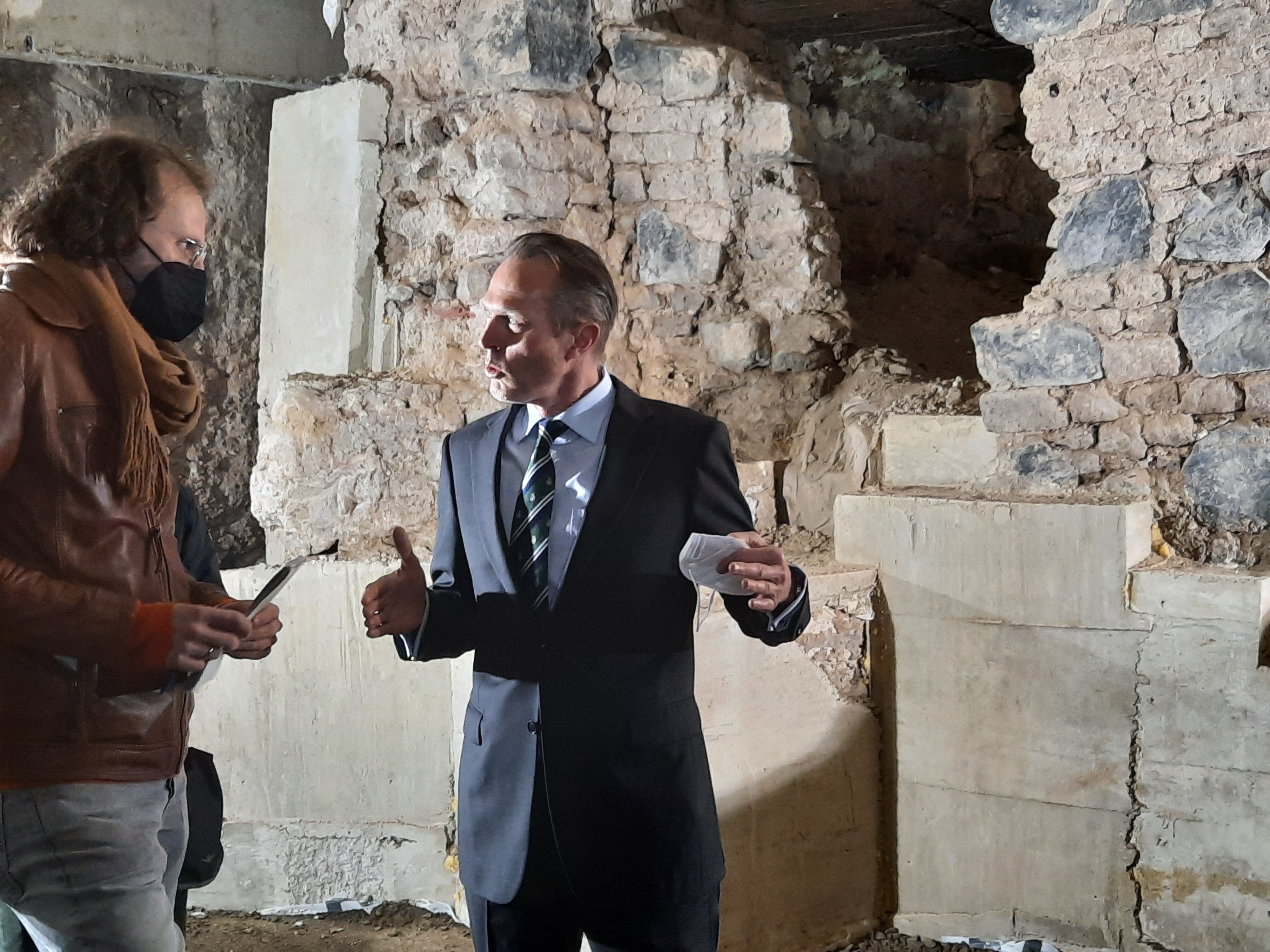 Zwei Männer, einer davon Thomas Otten, der Direktor des MiQua, sprechen miteinander. Im Hintergrund die archäologischen Befunde.