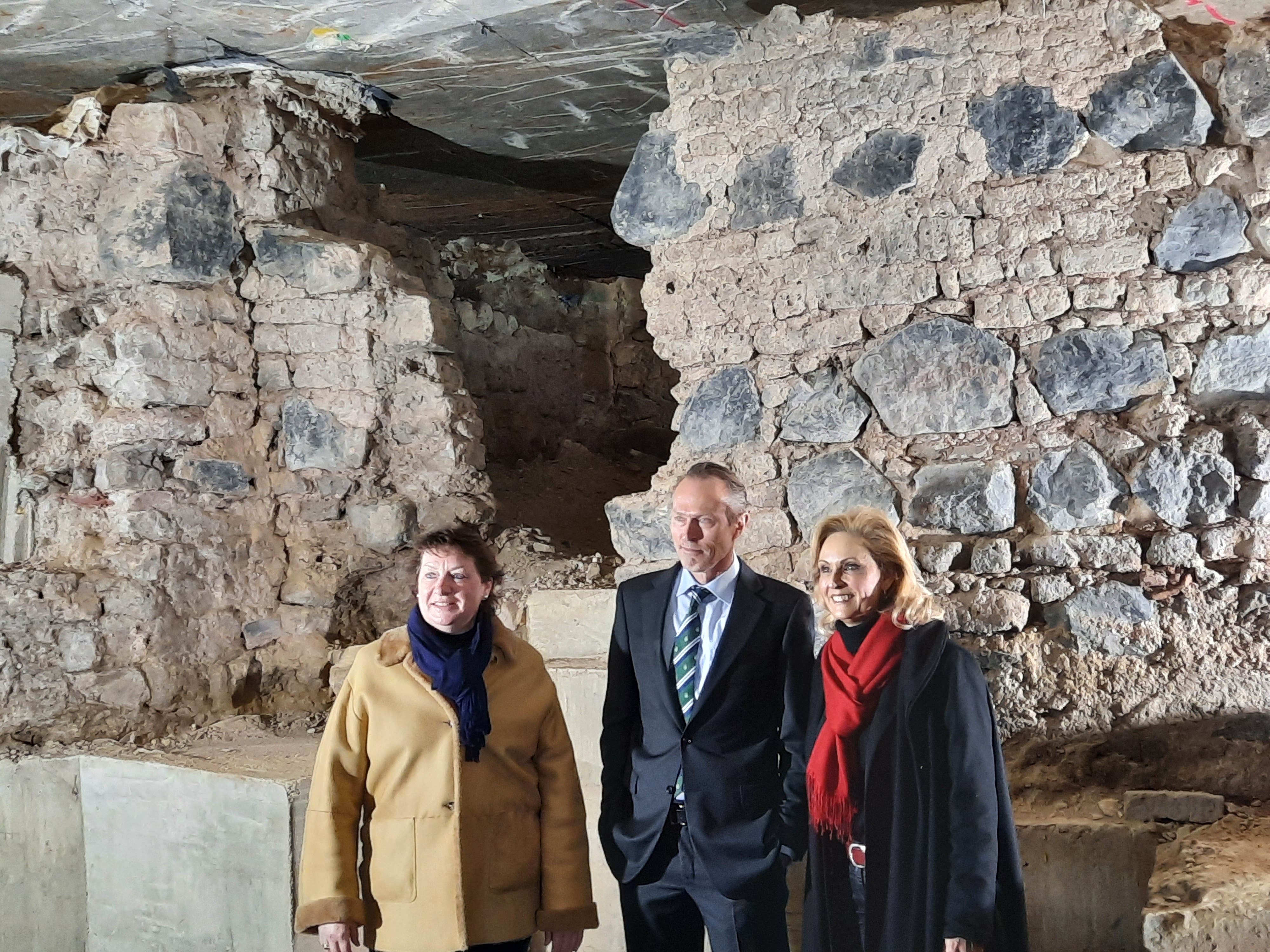 Anne Henk-Holstein, Thomas Otten und Ulrike Lubek stehen vor dem archäologischen Befund und lächeln in eine Kamera links von den Betrachter*innen des Bildes.