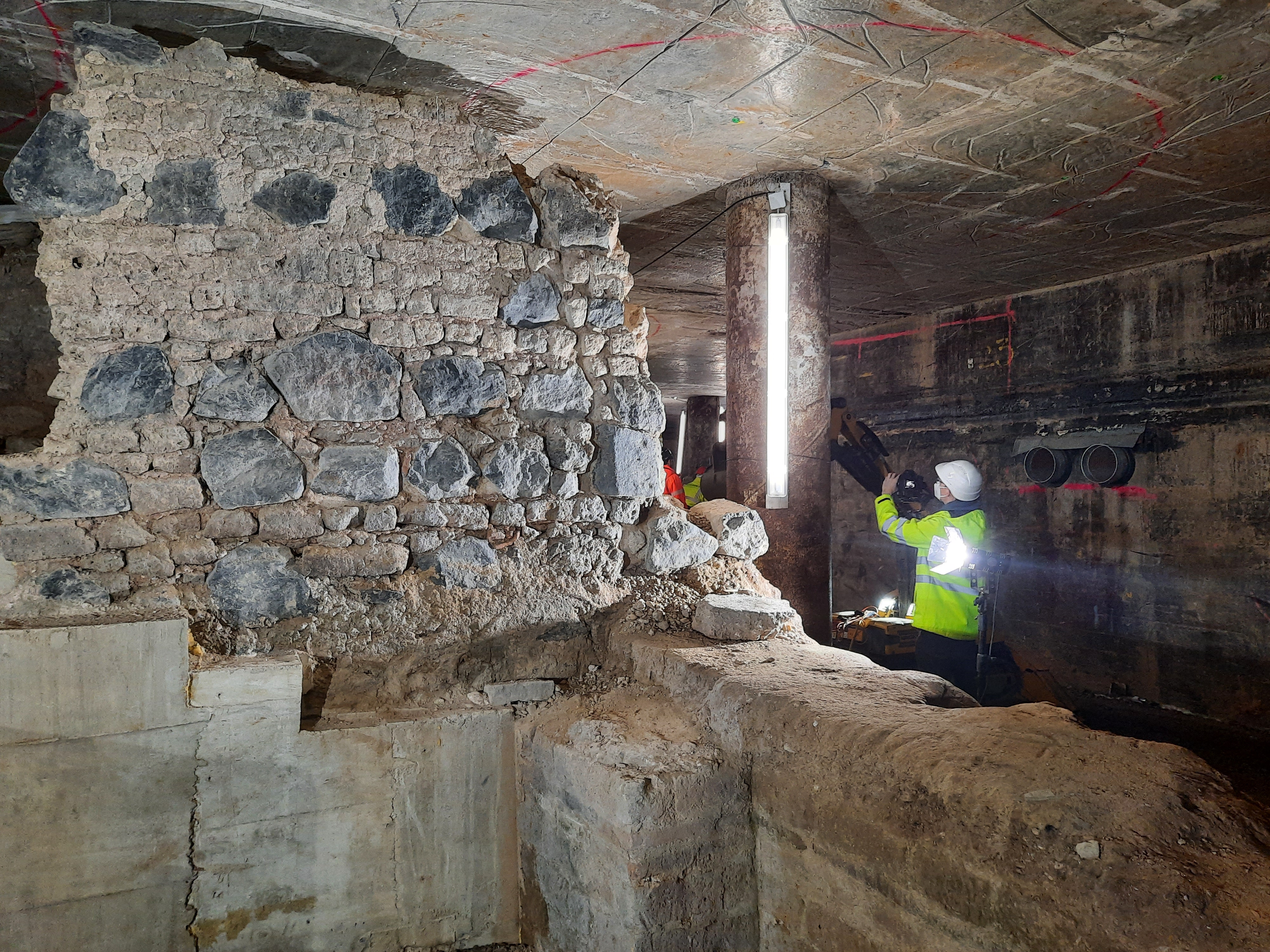 Archäologischer Befund als Fotomotiv. Rechts im Bild ein Fotograf mit Warnjacke und Bauhelm.