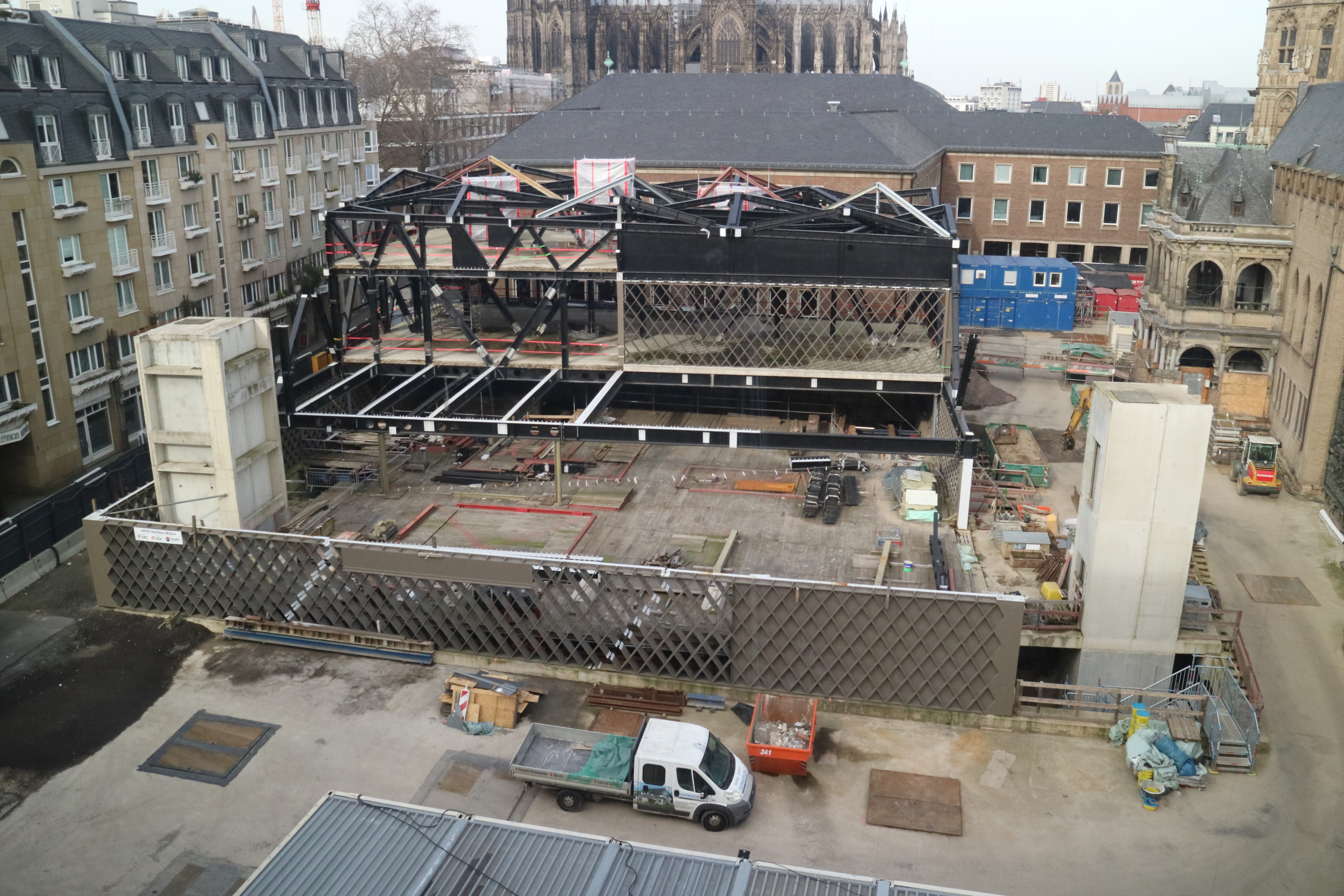 Die MiQua-Baustelle am 22. Februar 2023. In der Mitte die Stahlkonstruktionen des späteren Museumsbaus, drum herum die Rautentragwerke aus Stahl durch die später auch von außen schon ins Museum hineingeschaut werden kann. Vorne im Bild links und rechts die späteren Aufzugschächte als helle Betonsäulen.