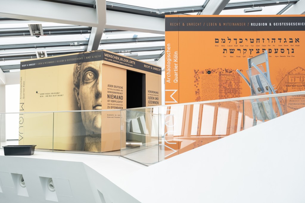 Zwei begehbare Ausstellungswürfel unter einem hellen Glasdach