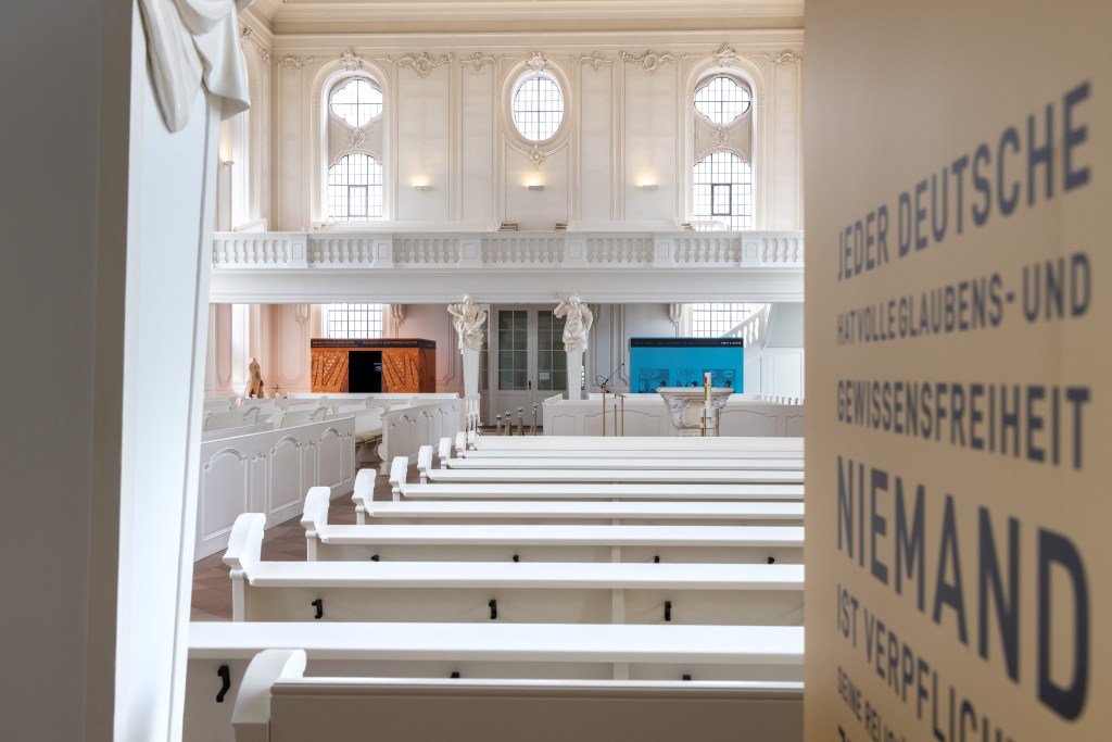 Zwei Ausstellungskuben im Inneren der weißen und mit Verzierungen ausgestatteten Ludwigskirche.