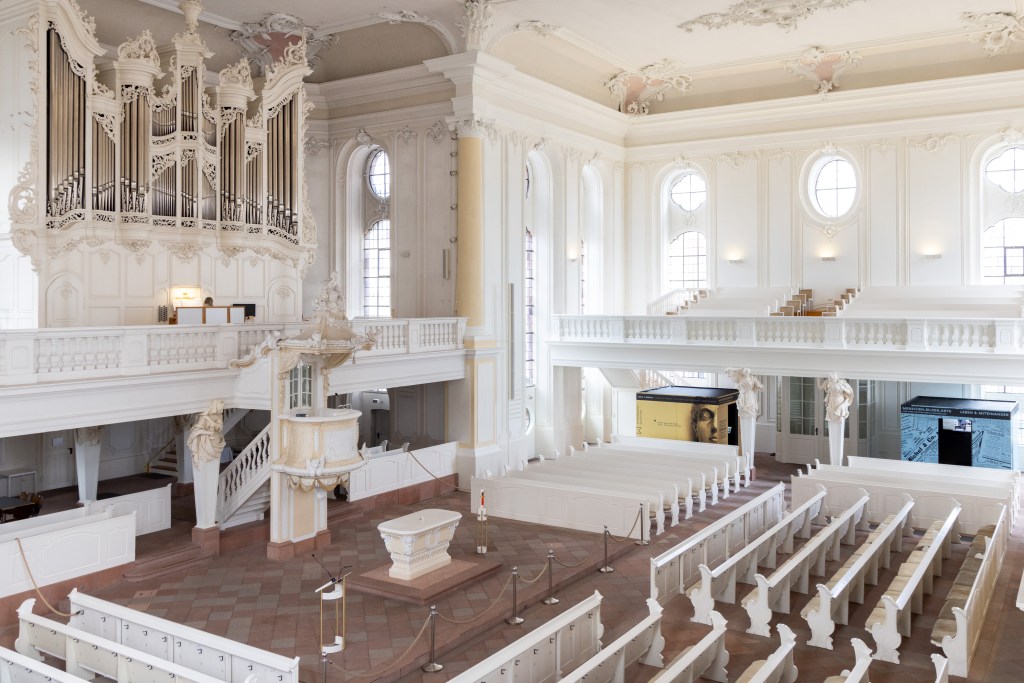 Zwei Ausstellungskuben im Inneren der weißen und mit Verzierungen ausgestatteten Ludwigskirche.