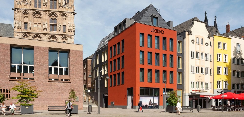 Ein signalrotes Haus am Alter Markt in Köln. Links daneben das Rathaus mit dem historischen Rathausturm