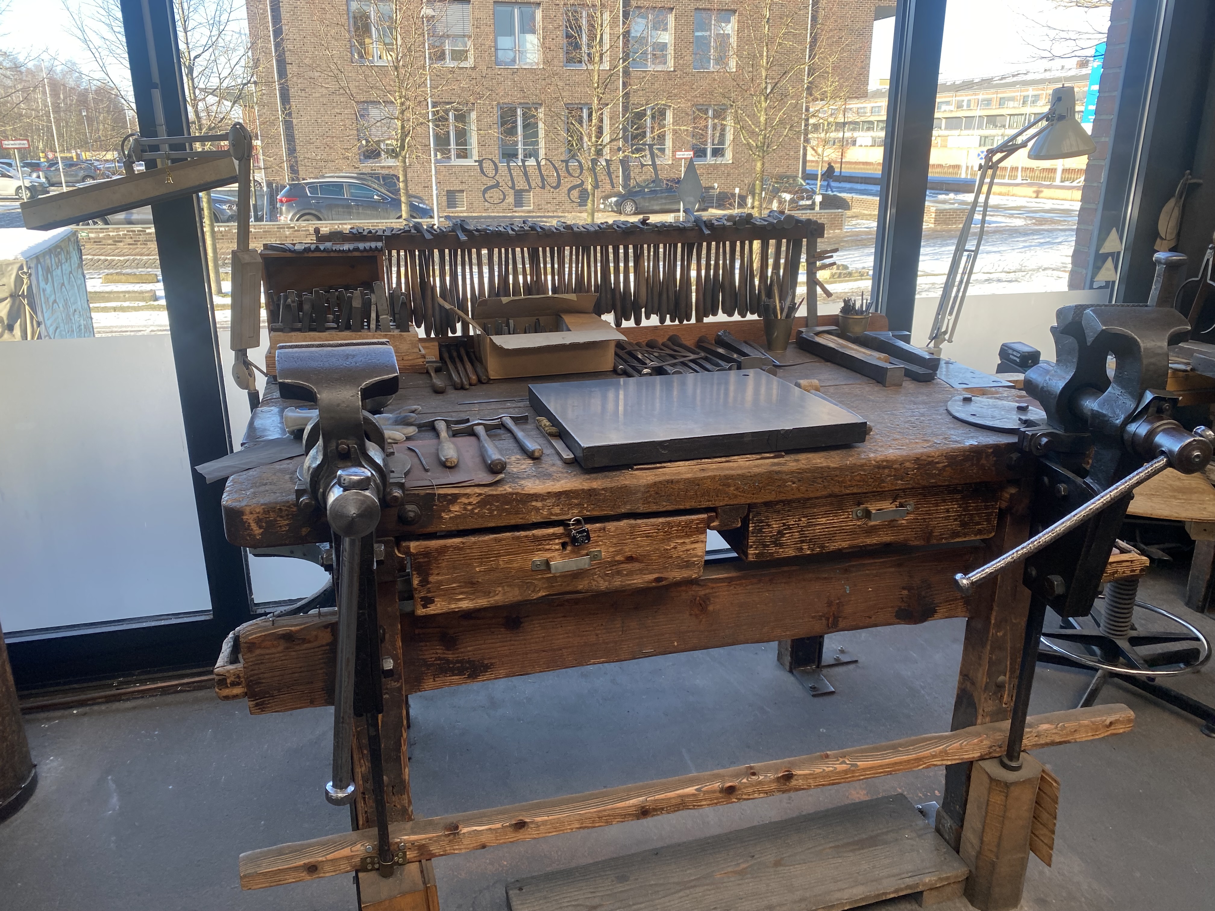 Das Bild zeigt einen Arbeitsplatz mit verschiedenen Werkzeugen, die auf einem Holztisch liegen.